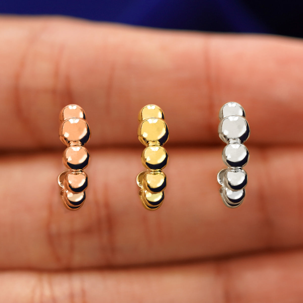 A model's hand holding three Graduated Puffy Beaded Hoops in between their fingers in rose, yellow, and white gold