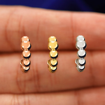 A model's hand holding three Graduated Puffy Beaded Hoops in between their fingers in rose, yellow, and white gold