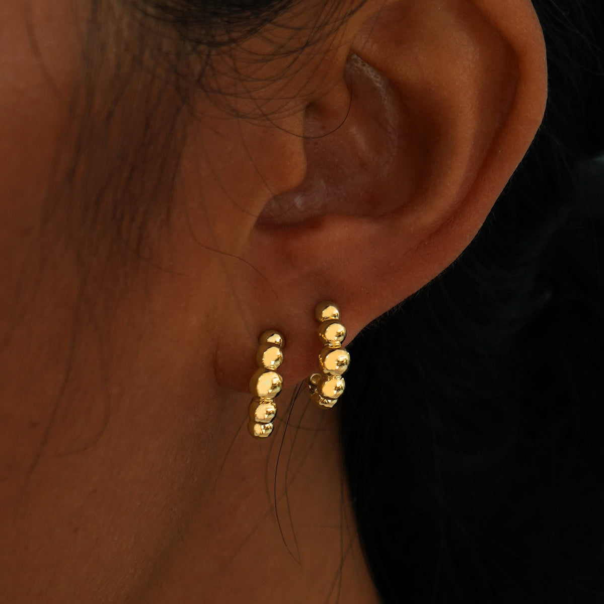 A model's ear wearing two yellow gold Graduated Puffy Beaded Hoops in two separate lobe piercings