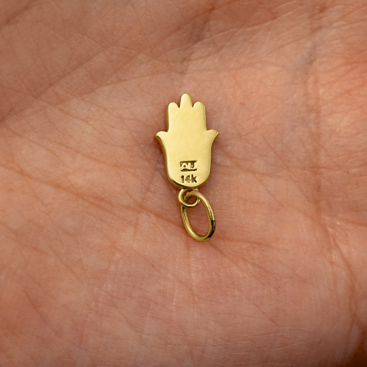 Back view of a solid 14k yellow gold Hamsa Charm resting on in the palm of a model's hand