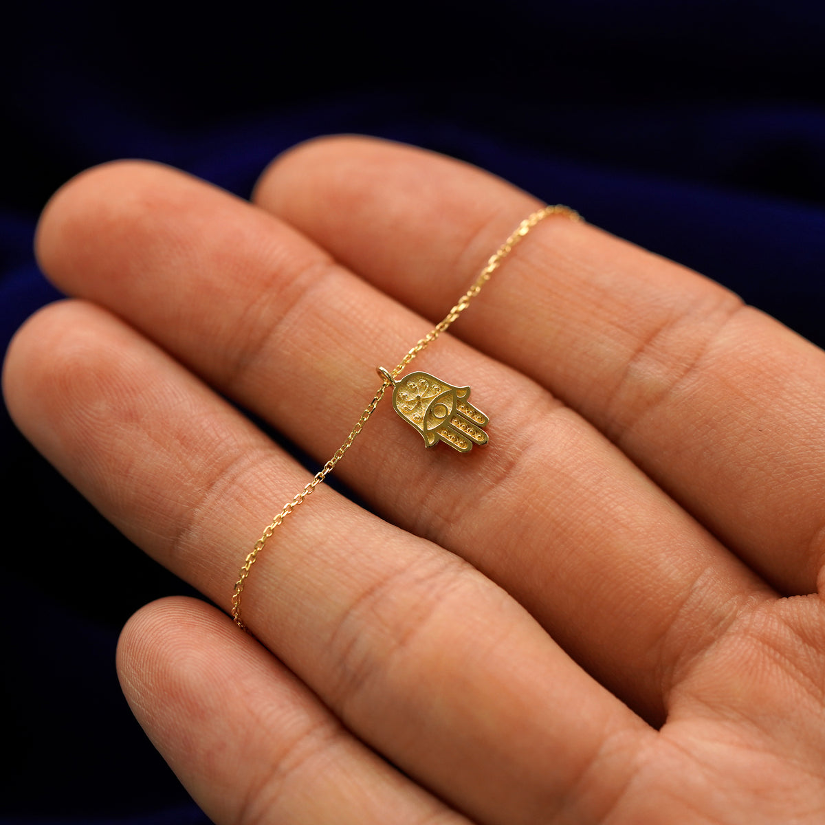 A 14k gold hamsa pendant necklace held across a model's fingertips to show details 