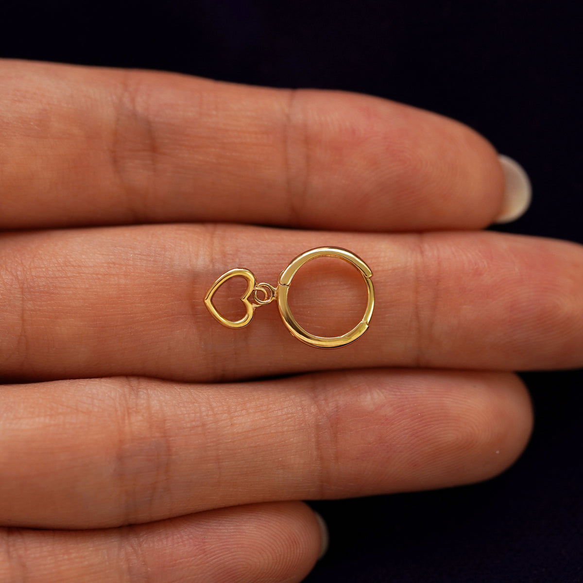 A solid 14k yellow gold Heart Dangle 
Huggie Hoop closed on a model's fingertips