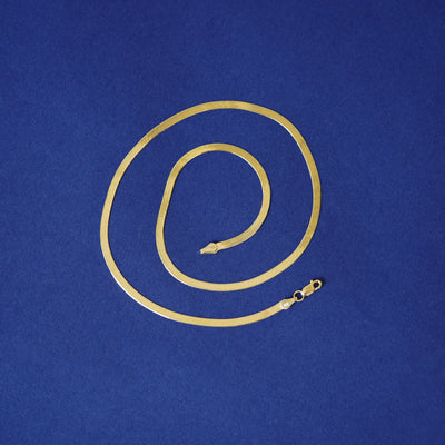 A 14k yellow gold herringbone chain necklace curled into a spiral on a blue background