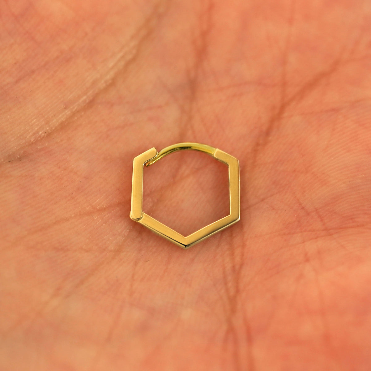 A closed single 14k yellow gold Hexagon Huggie Hoop resting in a model's palm