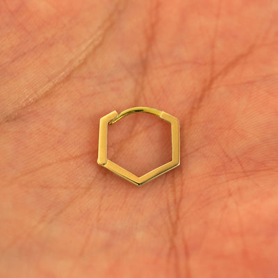 A closed single 14k yellow gold Hexagon Huggie Hoop resting in a model's palm