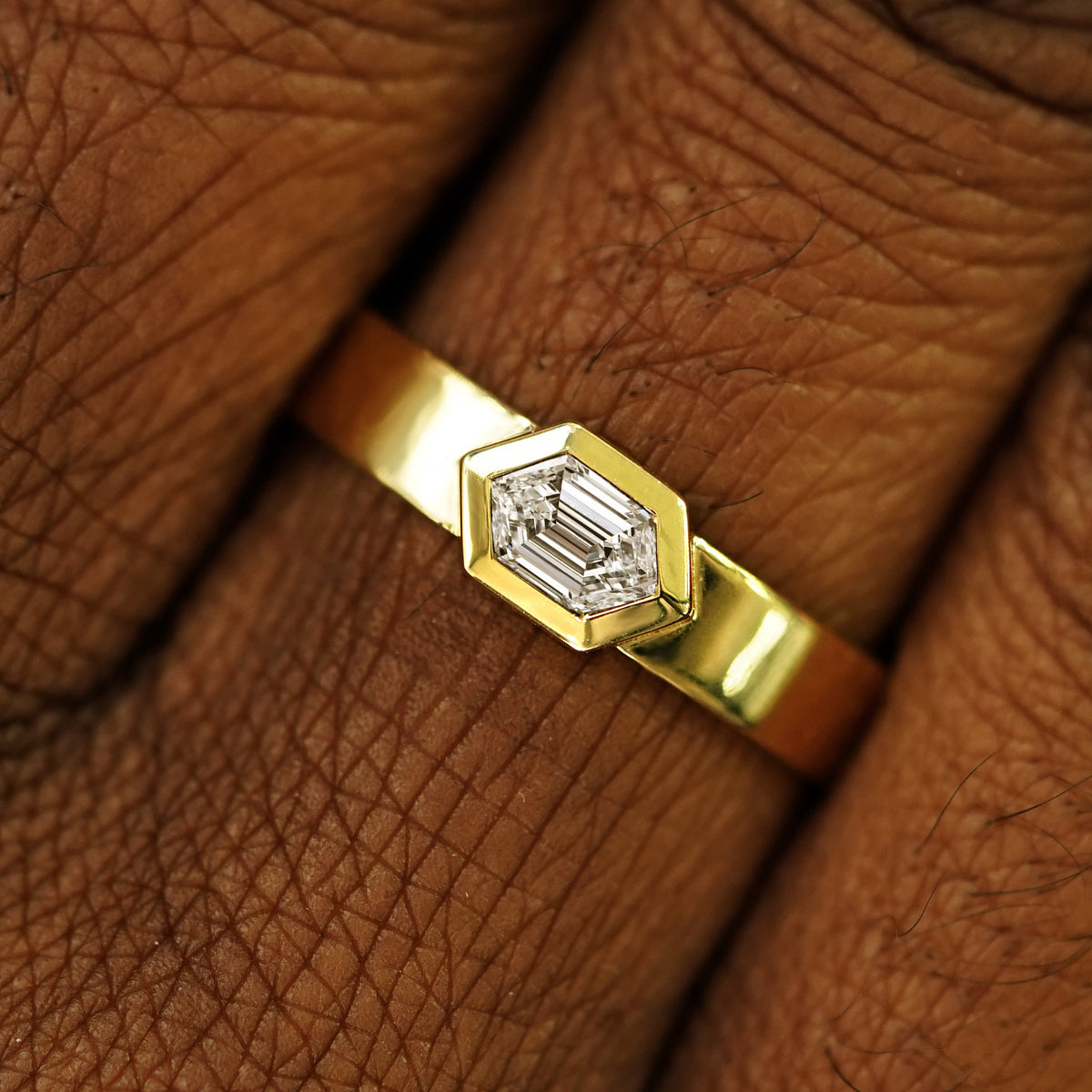Close up view of a model's hand wearing a solid yellow gold Hexagon Lab Clear Diamond Band