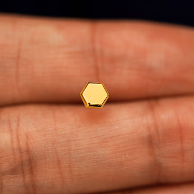 A solid 14k yellow gold Hexagon Earring in between a model's fingers