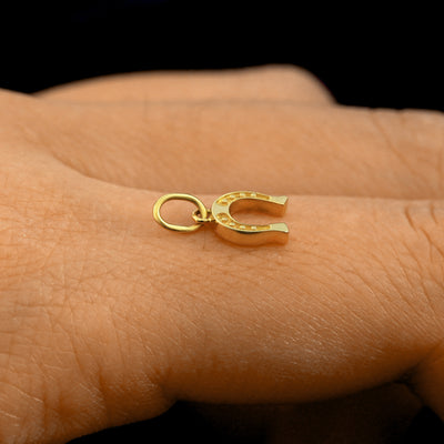 Side view of a 14k solid gold Horseshoe Charm on a model's finger to show the details and thickness of the charm