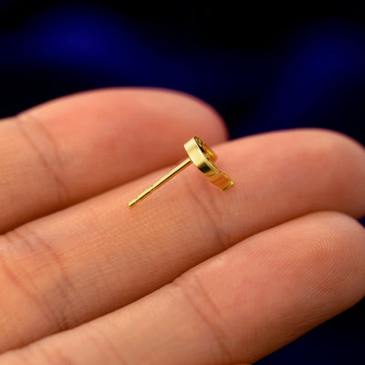 A 14k gold Horseshoe Earring in a model's hand resting on its side to show the thickness of the earring 