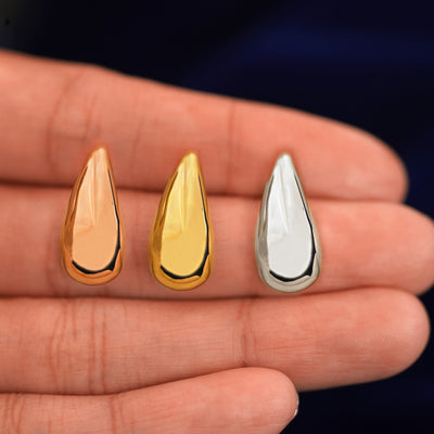 A model's hand holding three Teardrop puffy earrings in between their fingers in rose, yellow, and white gold