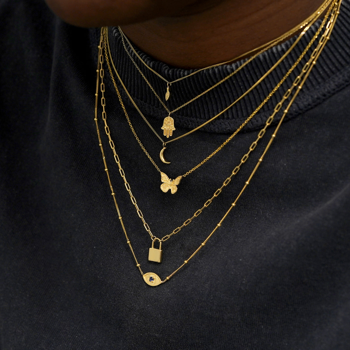 A model wearing seven different yellow gold charm necklaces layered