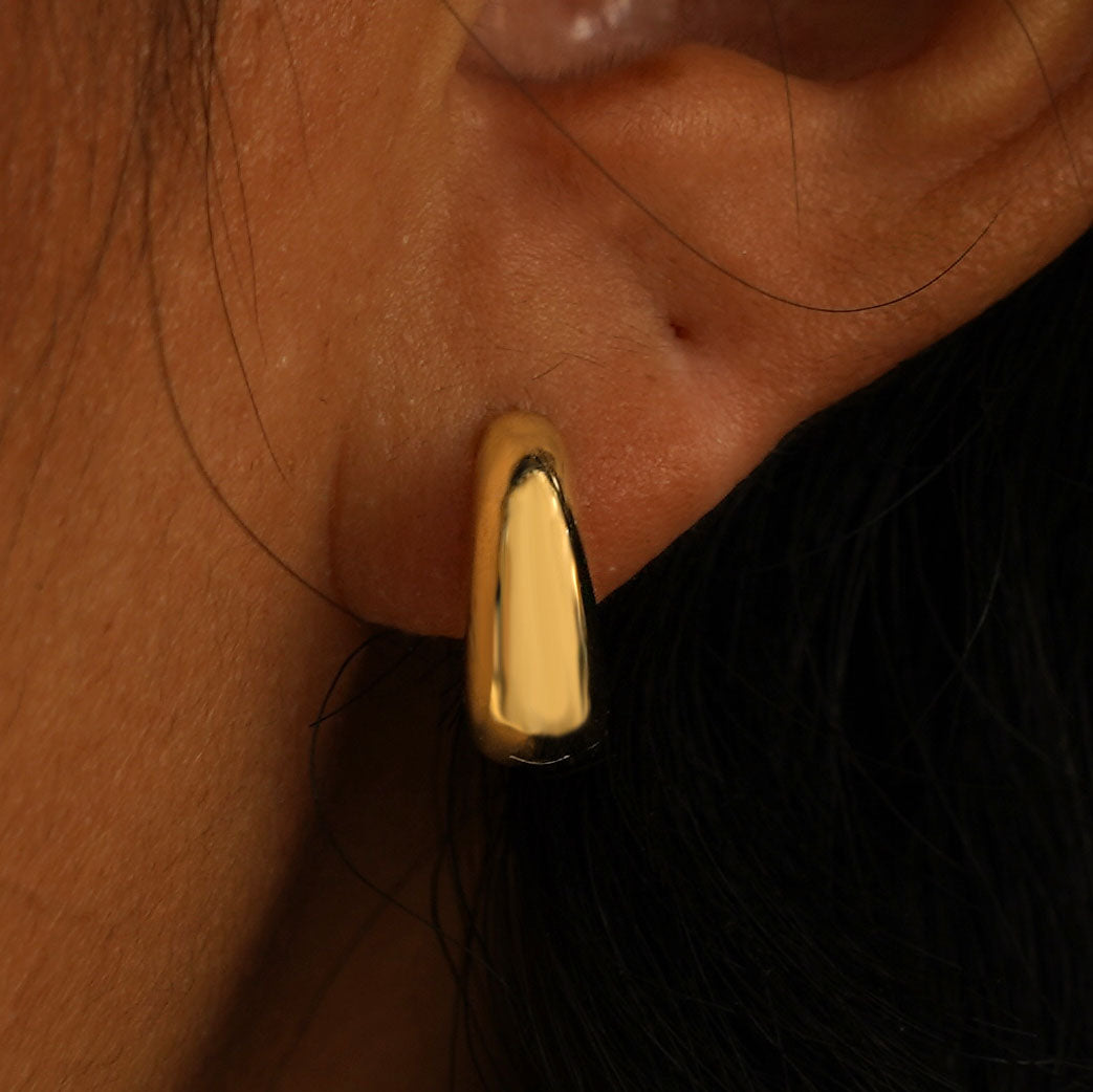 Close up view of a model's ear wearing a solid yellow gold Medium Teardrop Huggie Hoop
