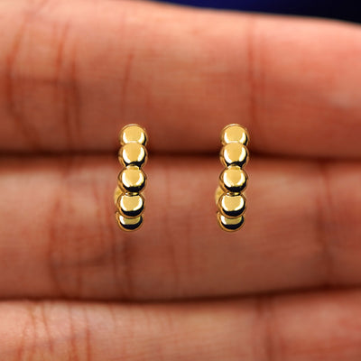 A model's hand holding a pair of 14k yellow gold Mini Puffy Beaded Hoops in between their fingers