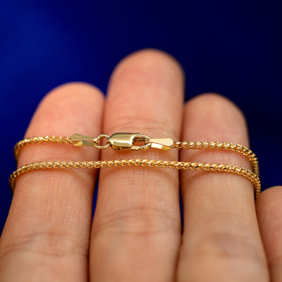 A yellow gold Mini Franco Chain Bracelet wrapped around a model's fingers to show the chain and the lobster claw clasp
