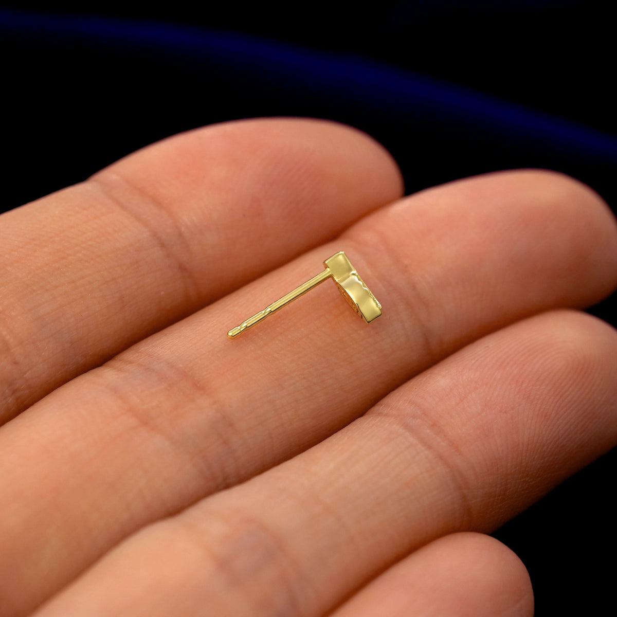A 14k gold Mini Leaf Earring in a model's hand resting on its side to show the thickness of the earring 