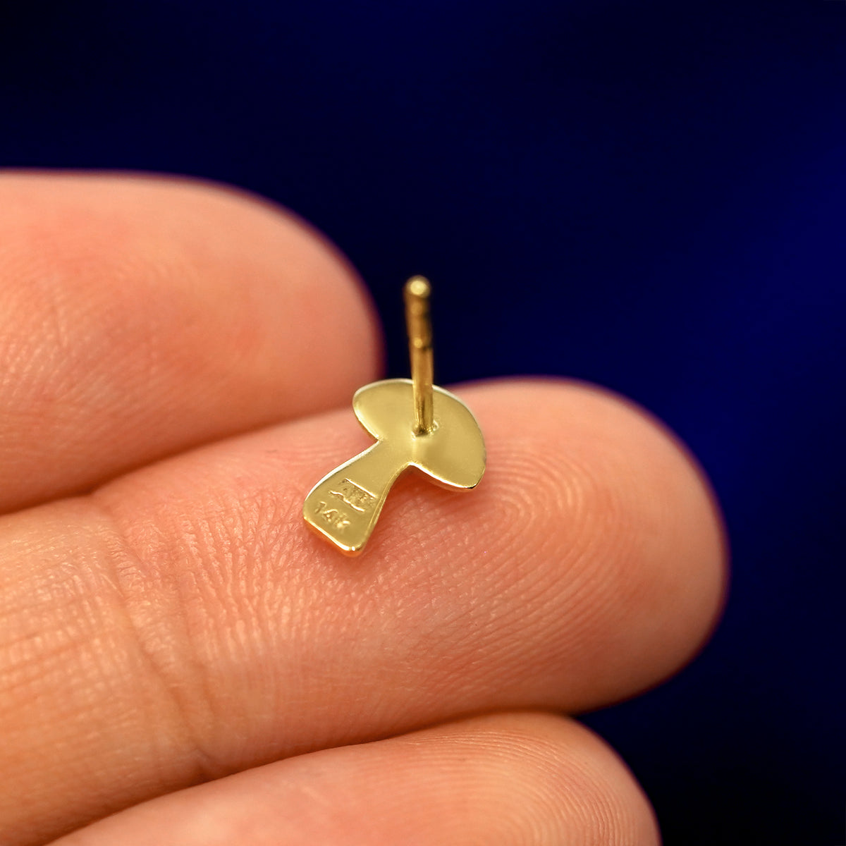 A 14k gold Mushroom Earring in a model's hand resting on its face  to show the back of the stud and the post