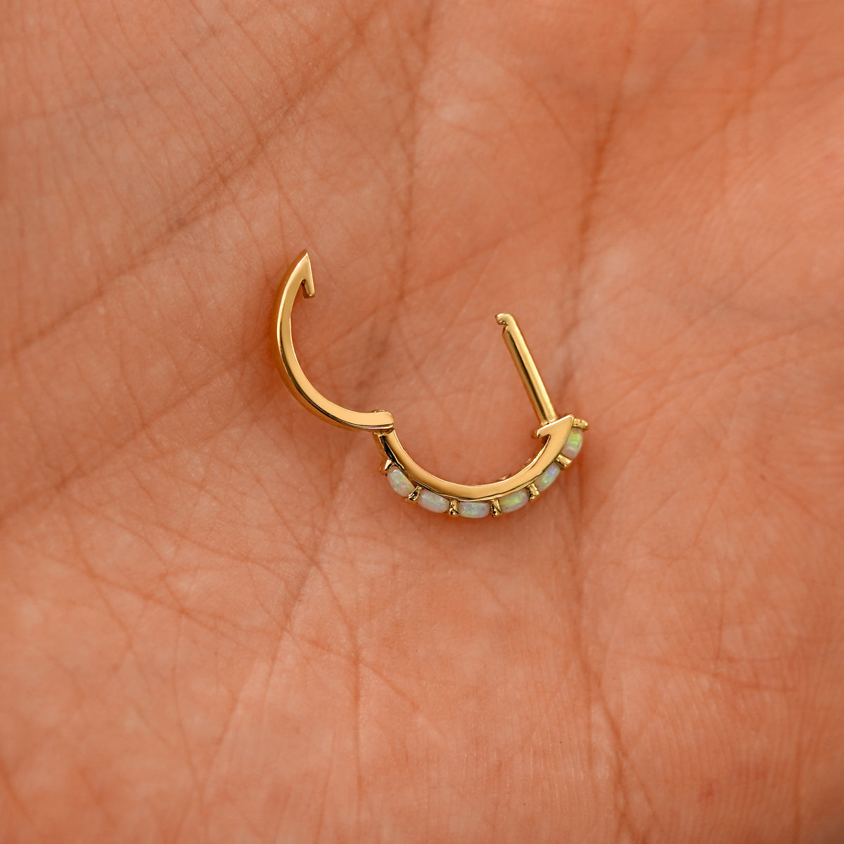 An open Opal huggie hoop laying in a models palm
