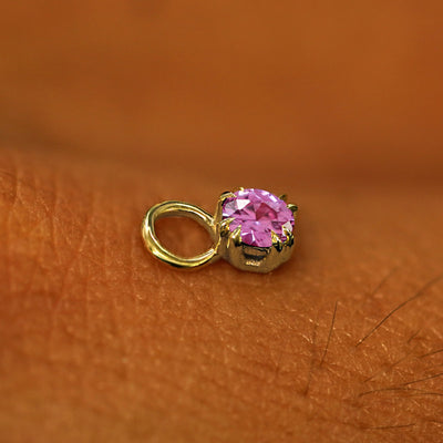 A solid yellow gold Pink Sapphire Charm for earring resting on the back of a model's hand