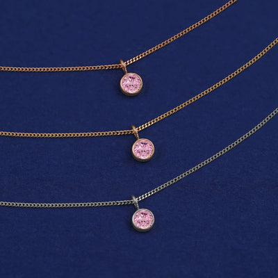 Three versions of the Pink Sapphire Necklace shown in options of yellow, white and rose gold on a dark blue background