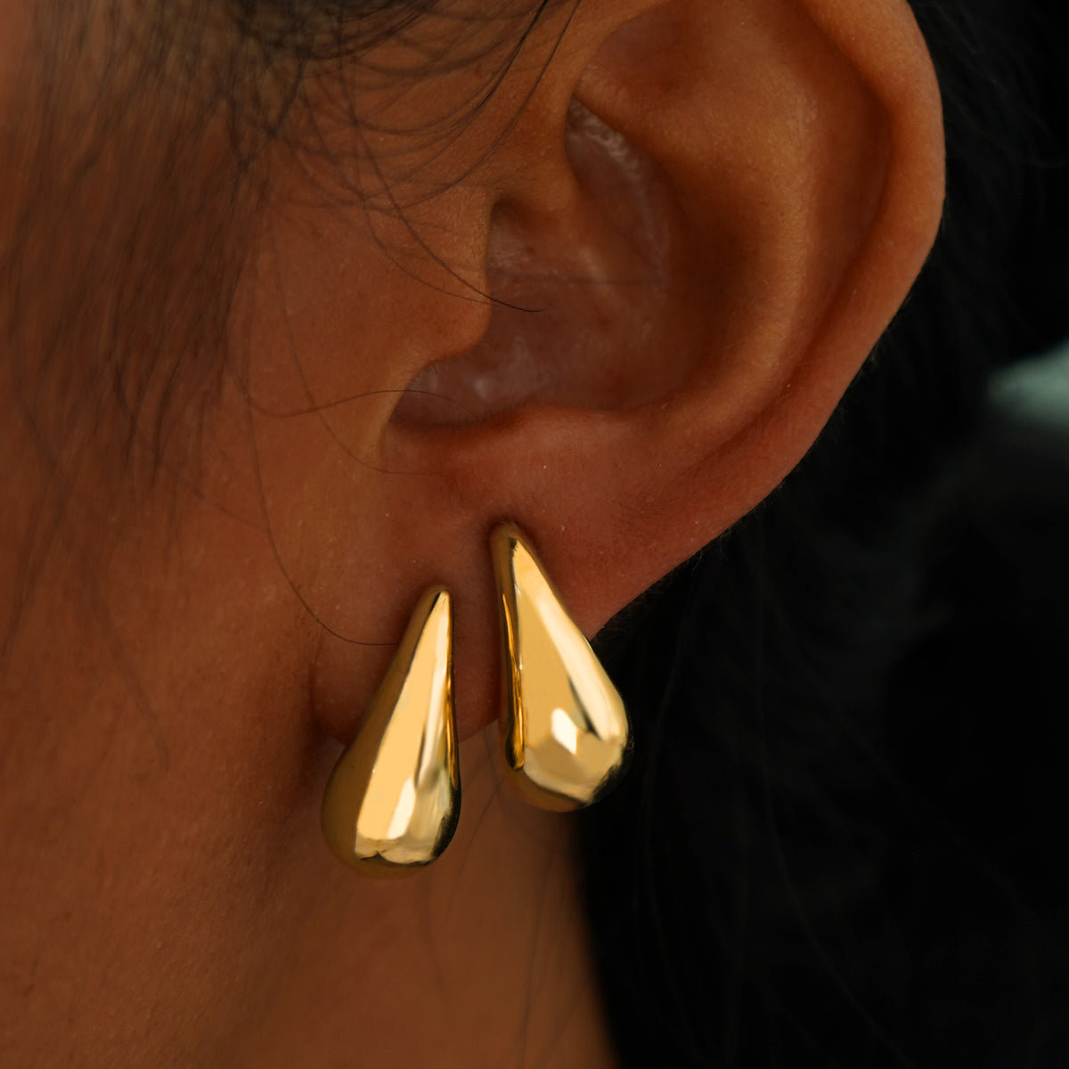 A model's ear wearing two yellow gold Teardrop Puffy Earrings in two separate lobe piercings