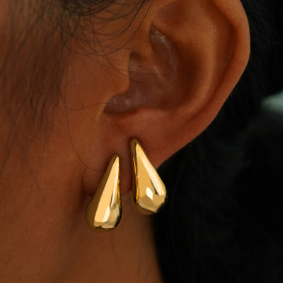 A model's ear wearing two yellow gold Teardrop Puffy Earrings in two separate lobe piercings