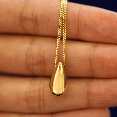 A Puffy Teardrop Necklace laying over a model's fingertips to show the details of the back view