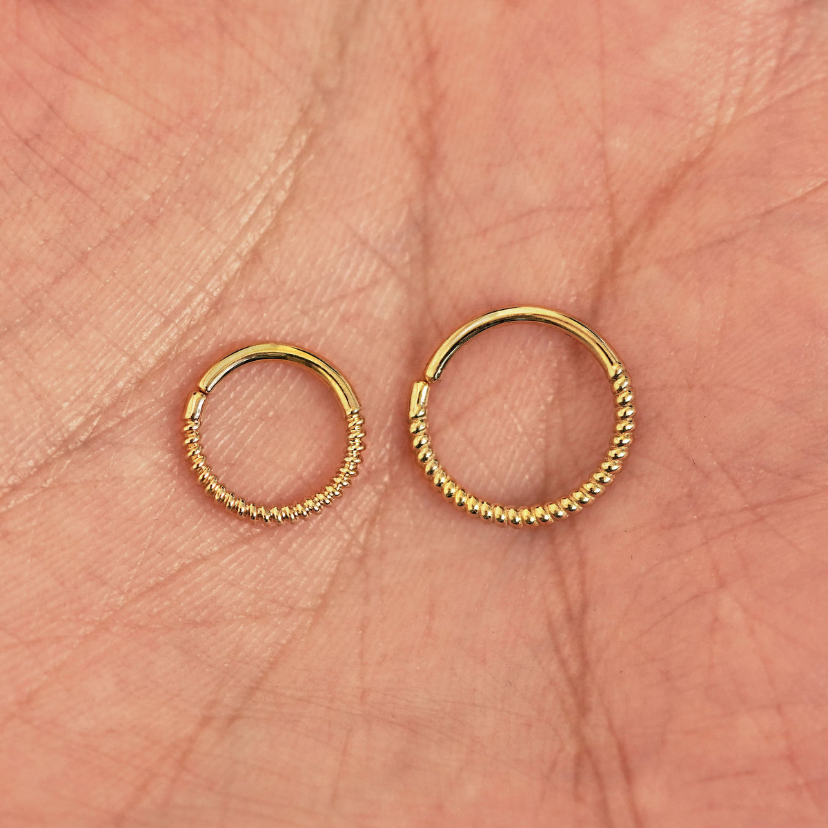 A model's palm holding two versions of the pierced Rope Septum showing the 8mm and 10mm sizes