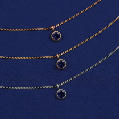 Three versions of the Sapphire Necklace in options of yellow, white, and rose gold on a dark blue background