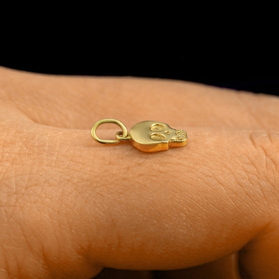 Side view of a 14k solid gold Skull Charm on the back of a model's finger to show the details and thickness of the charm