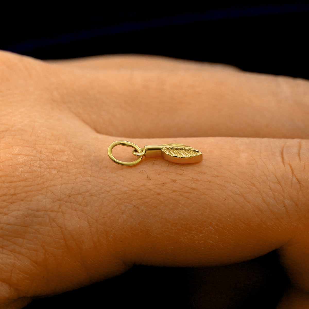 Side view of a 14k solid gold Leaf Charm on a model's finger to show the details and thickness of the charm