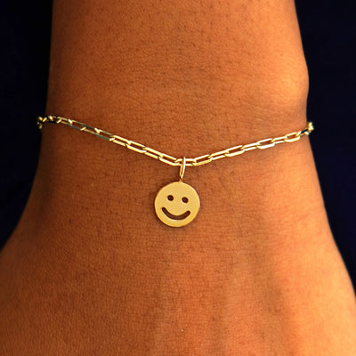 Close up view of a model's wrist wearing a yellow gold Smiley Face Charm on a Butch Chain Bracelet