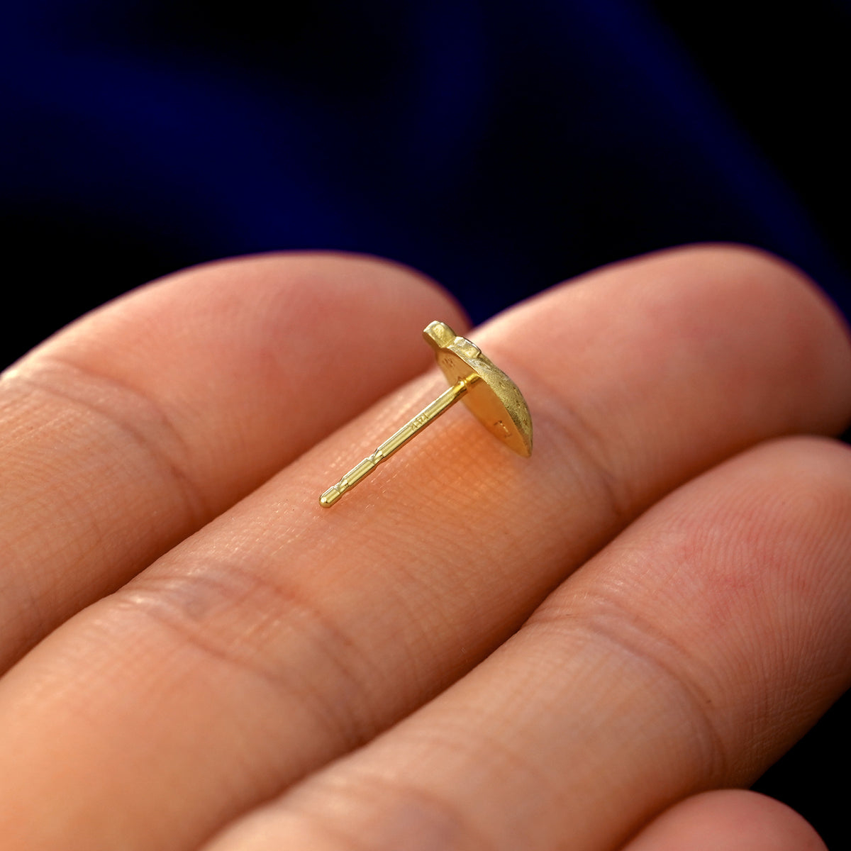 A 14k gold Strawberry Earring in a model's hand resting on its side to show the thickness of the earring 