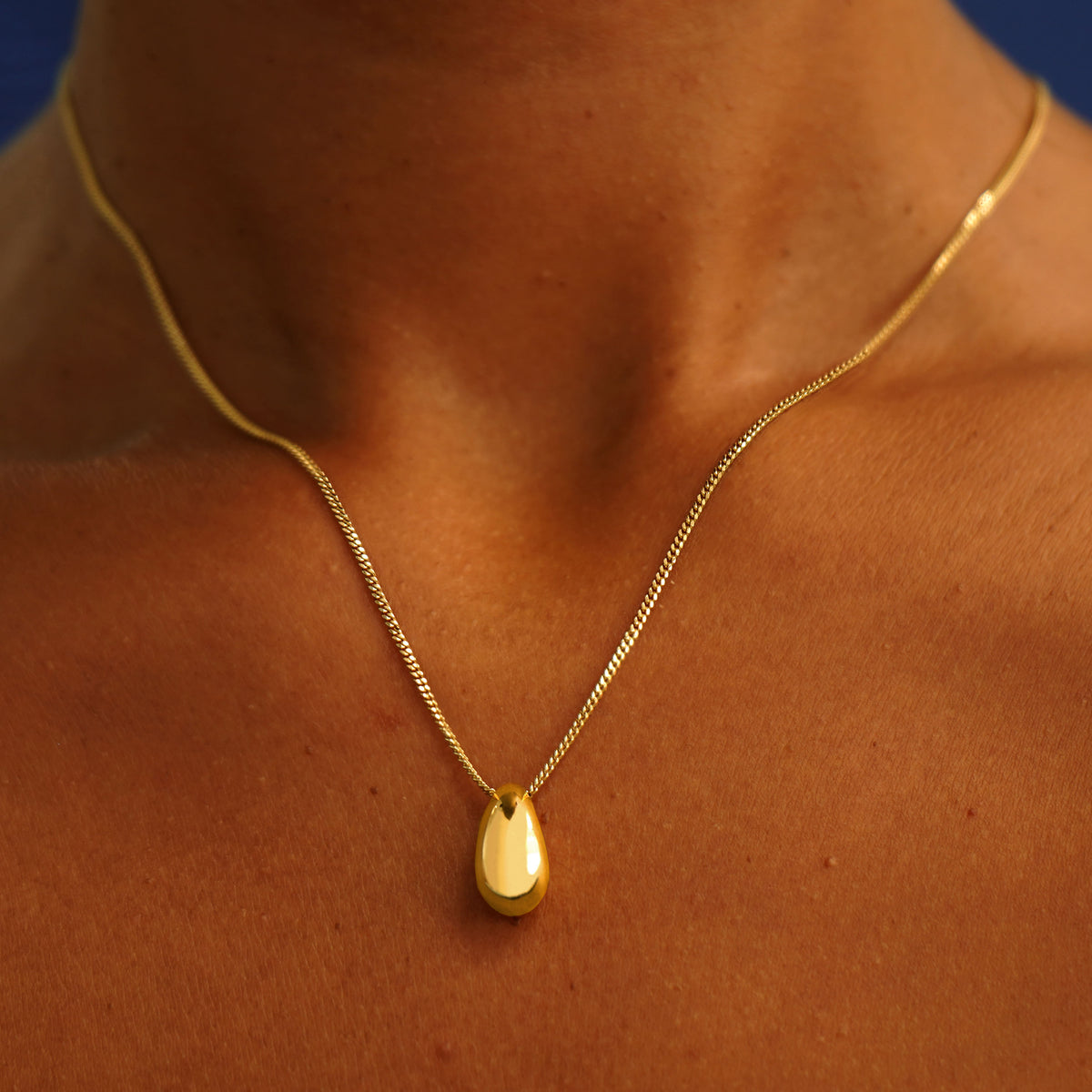 A model's neck wearing a 14k gold Puffy Teardrop Necklace