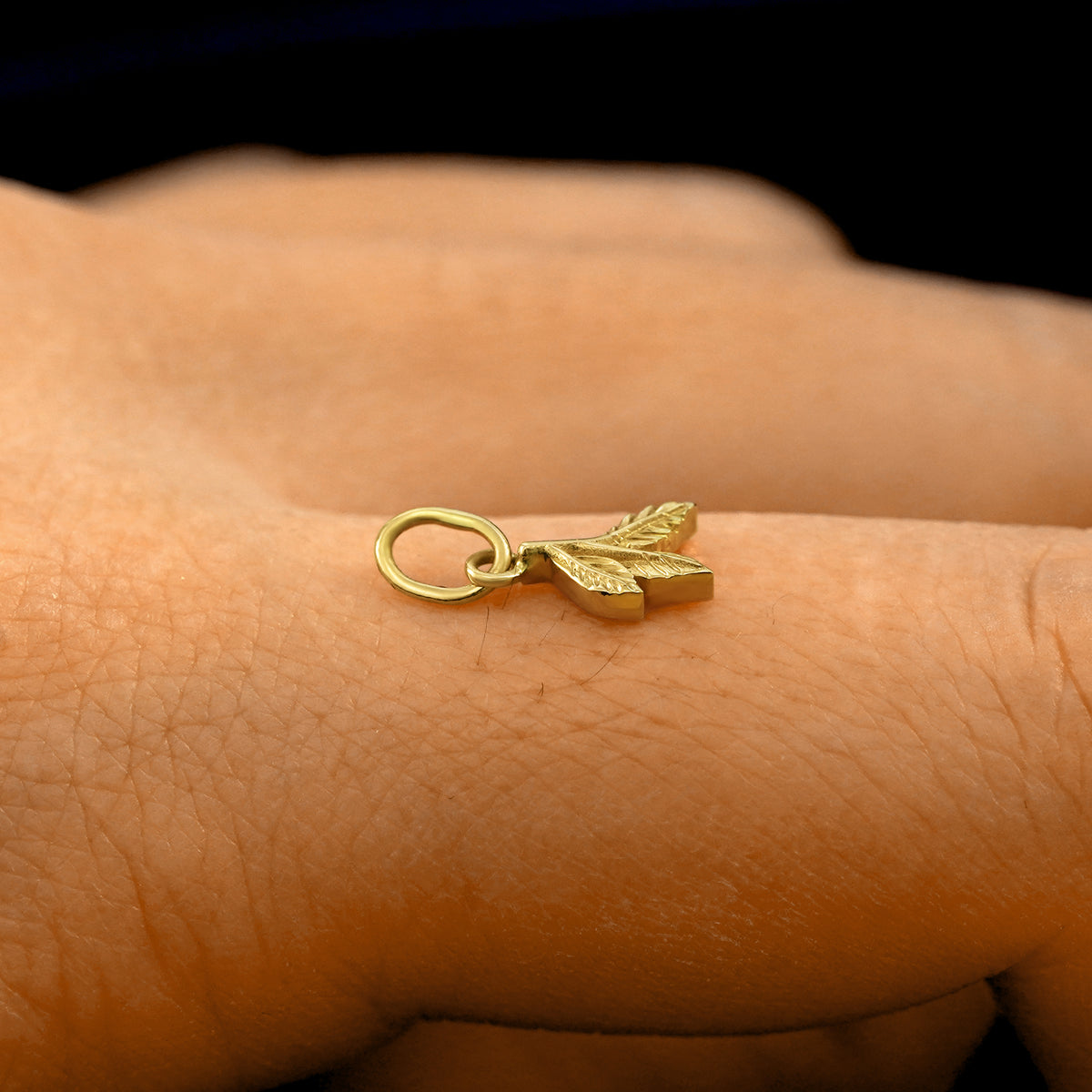 Side view of a 14k solid gold 3 Leaves Charm on a model's finger to show the details and thickness of the charm