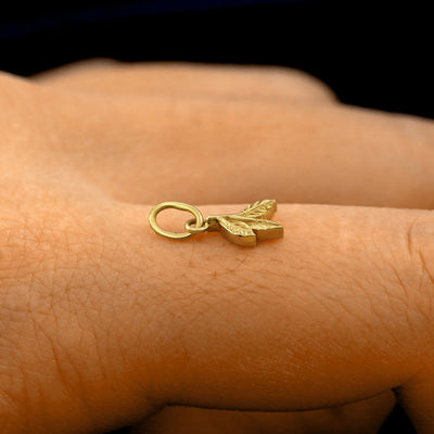 Side view of a 14k solid gold 3 Leaves Charm on a model's finger to show the details and thickness of the charm