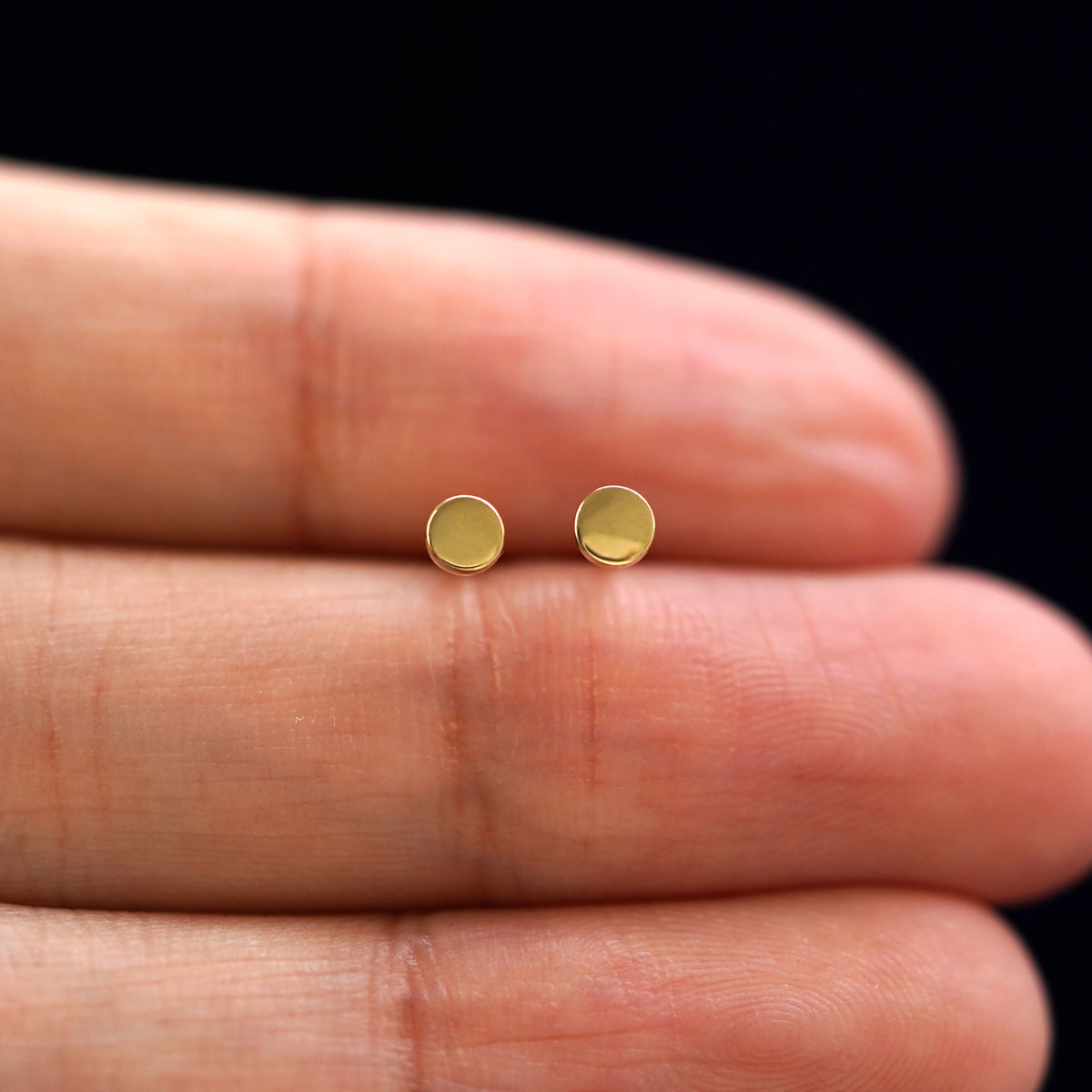 A model's hand holding a pair of recycled 14k gold Small Circle Earrings