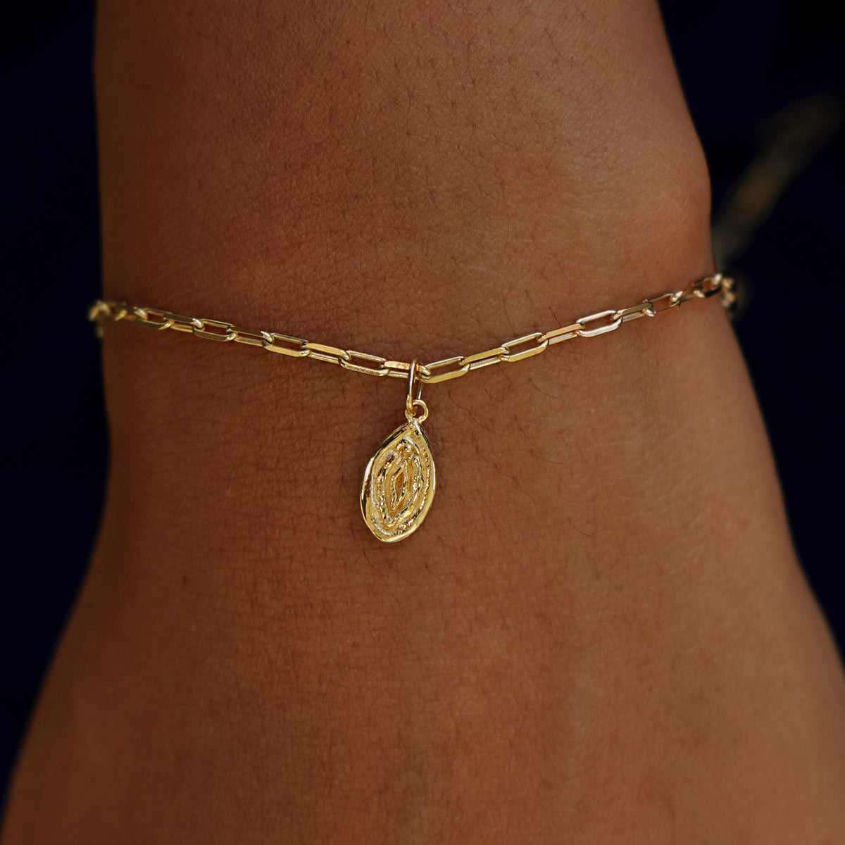A model's wrist wearing a yellow gold Vulva Charm on a Butch Bracelet