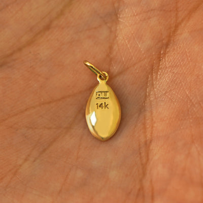 Back view of a solid gold Vulva Charm for chain resting in a model's palm