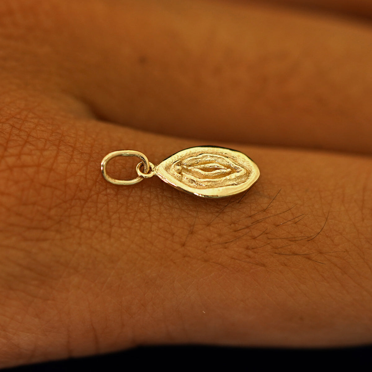 A 14k solid gold Vulva Charm for chain balancing on the back of a model's finger