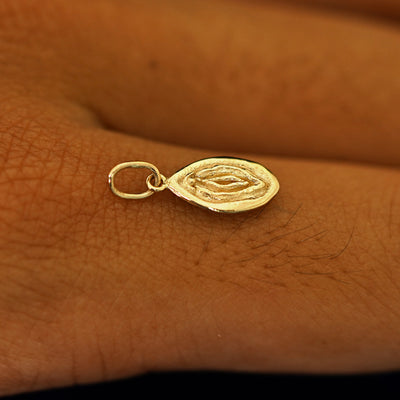 A 14k solid gold Vulva Charm for chain balancing on the back of a model's finger