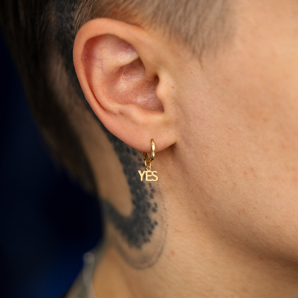 Close up view of a model's ear wearing a solid gold Yes Charm on a Curvy huggie hoop earring