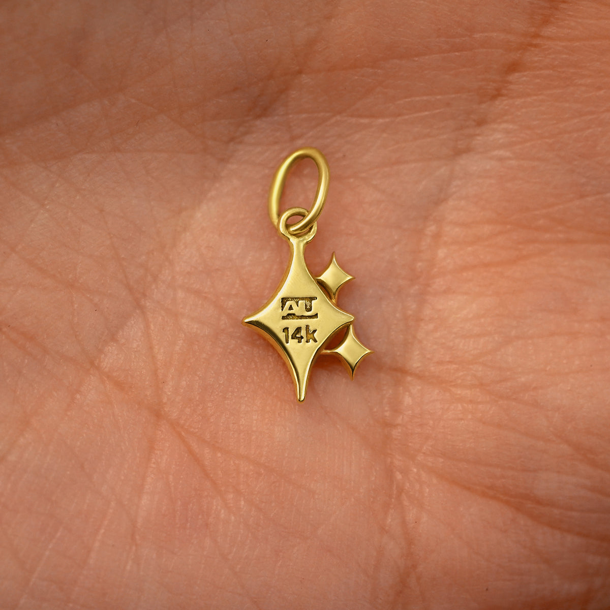Back view of a solid 14k yellow gold Sparkle Emoji Charm resting on in the palm of a model's hand