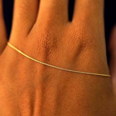 A solid gold Wheat Chain resting on the back of a model's hand