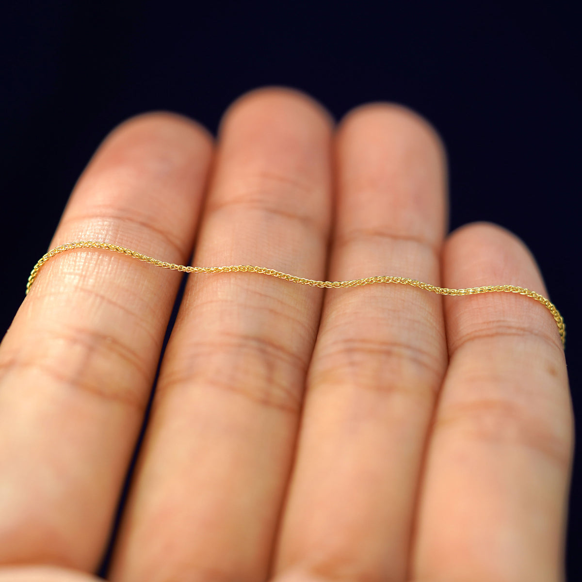 A yellow gold Wheat Chain resting on a model's fingers