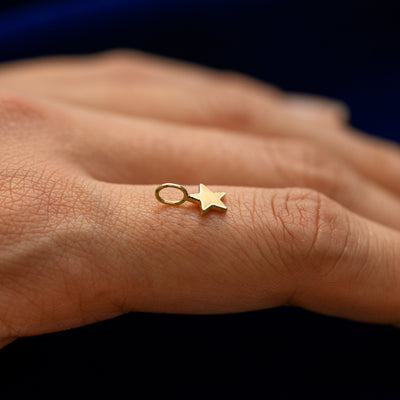 Side view of a for chain star charm resting on a models finger to show the thickness of the charm