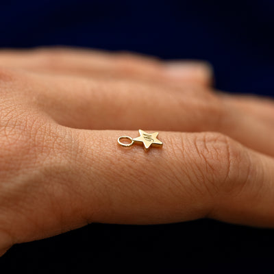 Side view of a for earring star charm resting on a models finger to show the thickness of the charm