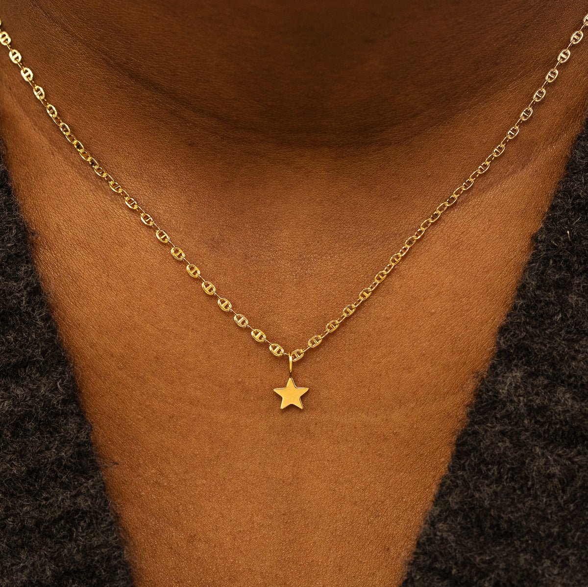 A model wearing a solid gold star charm on a mariner chain