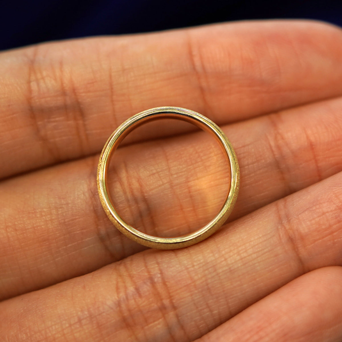 A yellow gold Mix Stardust Band in a model's hand showing the thickness of the band