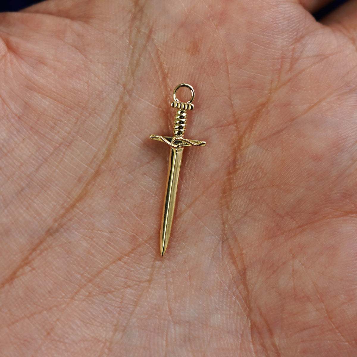 A 14k gold Sword Charm for earring resting in a model's palm to show the underside of the charm