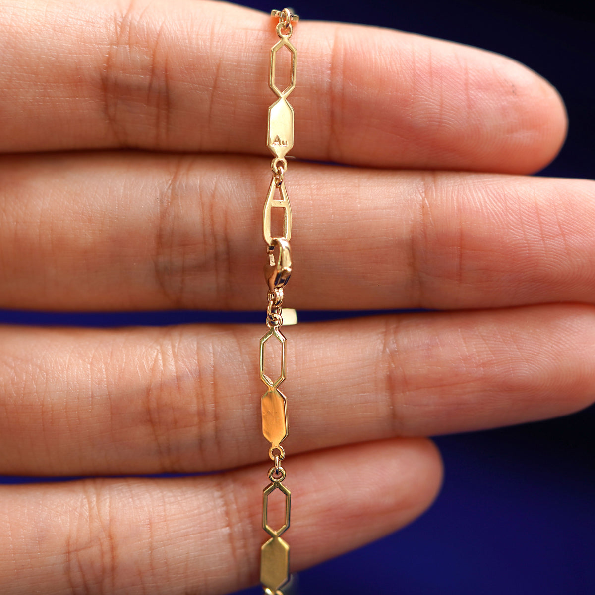 A model's hand holding an Automic Gold AU lobster claw lock on a yellow gold Tanlah Chain